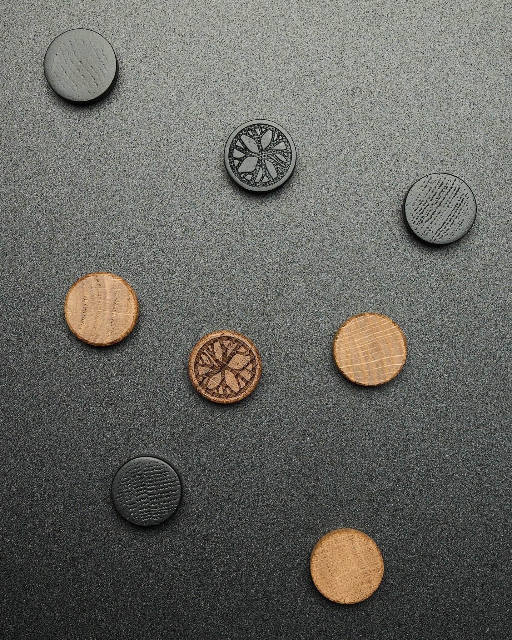 Fire runde black oak magneter fra WoodUpp Norr Magnet Set, løst arrangert på en teksturert mørk overflate, utformet som Akupanel tilbehør.